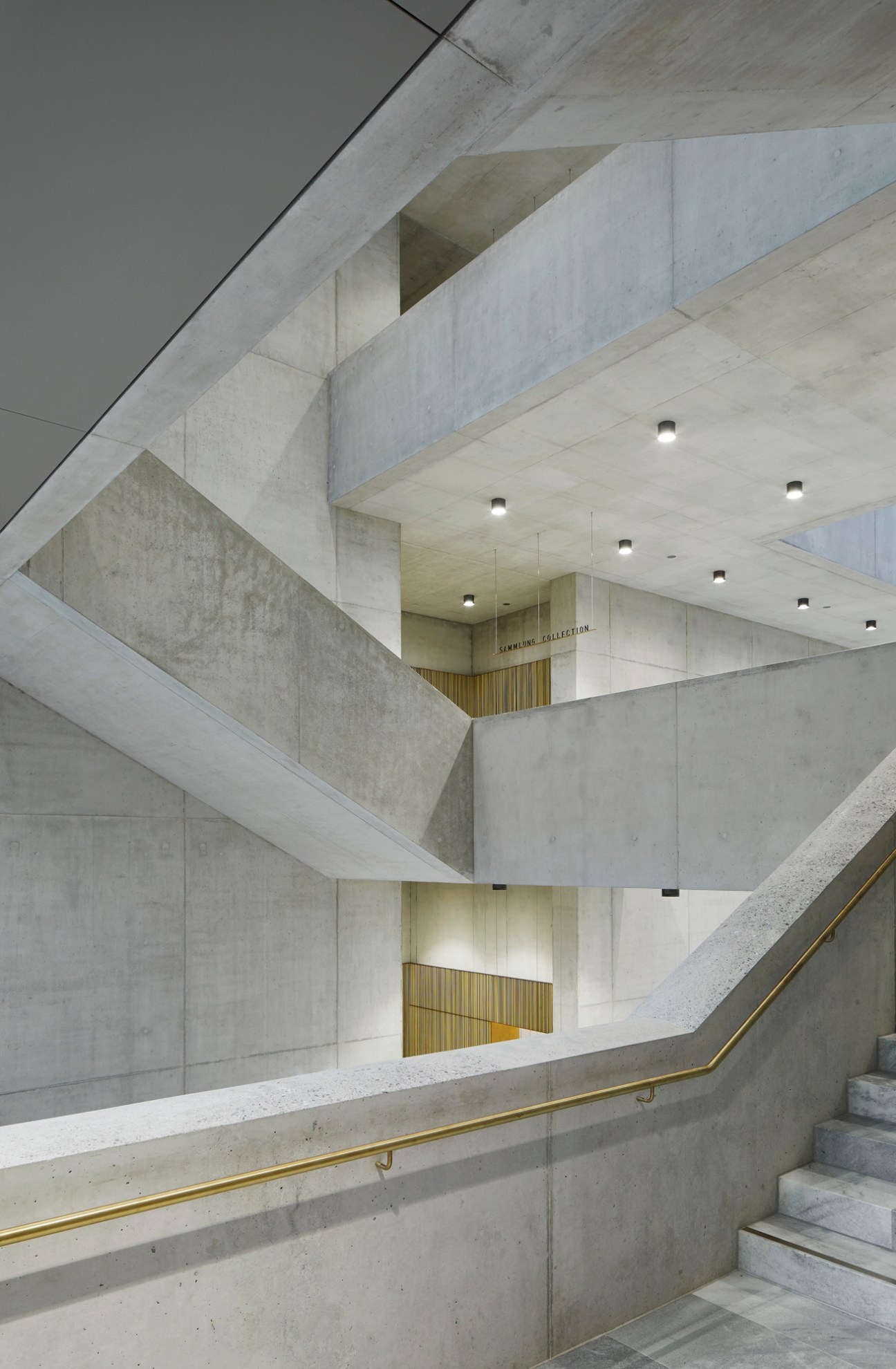 Museum interior staircase with concrete walls, brass handrails and recessed ceiling lighting