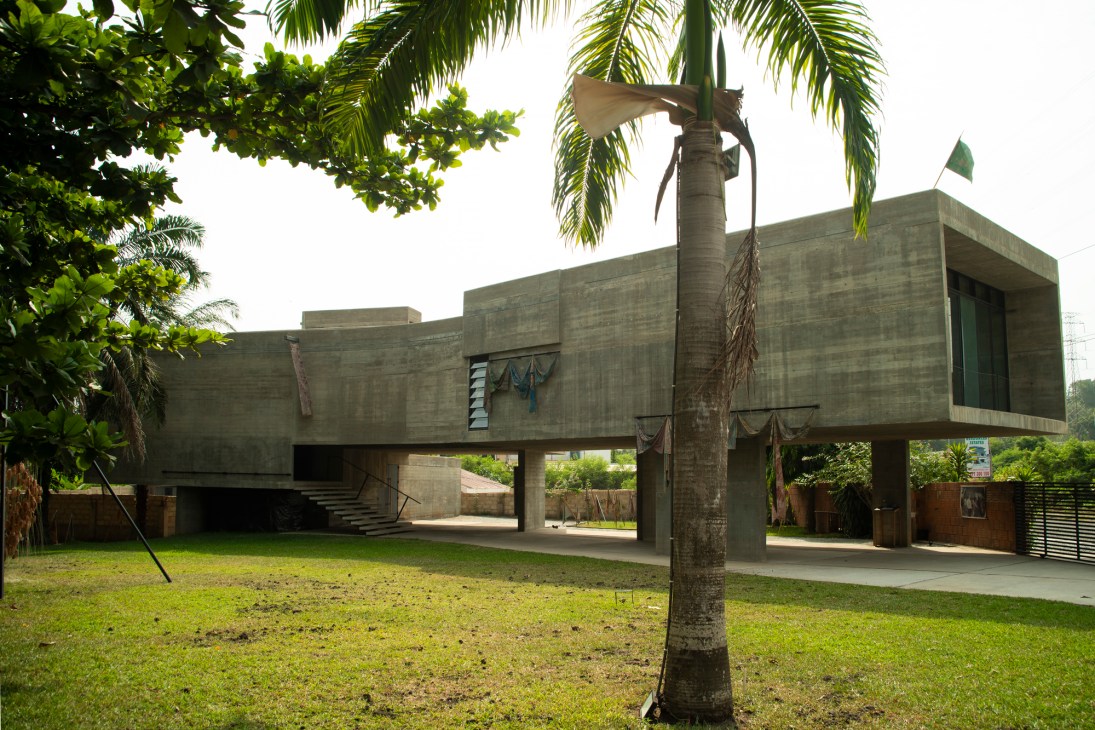 Modern concrete building elevated on pillars with palm tree and green lawn in foreground