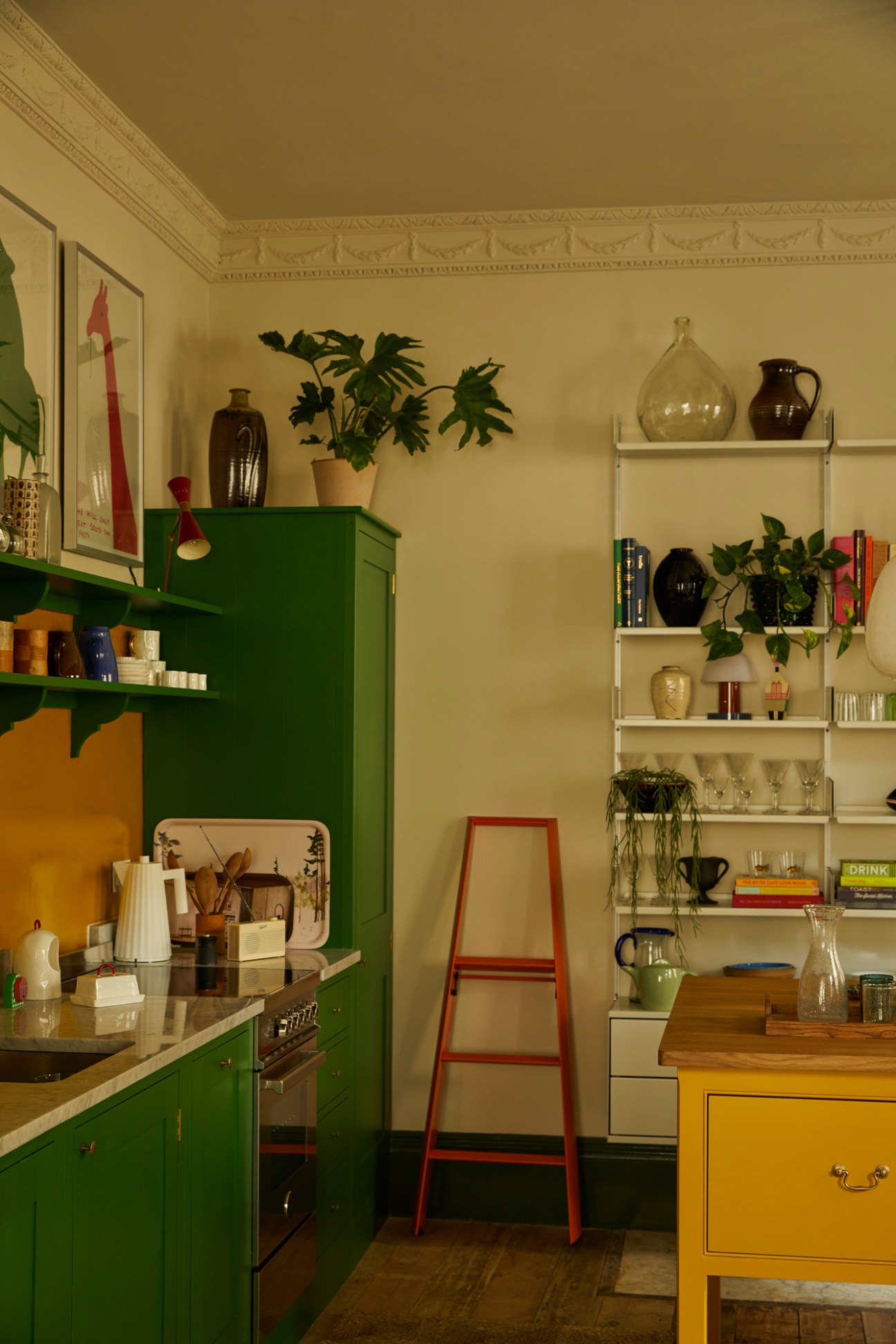 Kitchen with green cabinets, white shelving unit, plants, pottery and vintage design objects in Georgian townhouse
