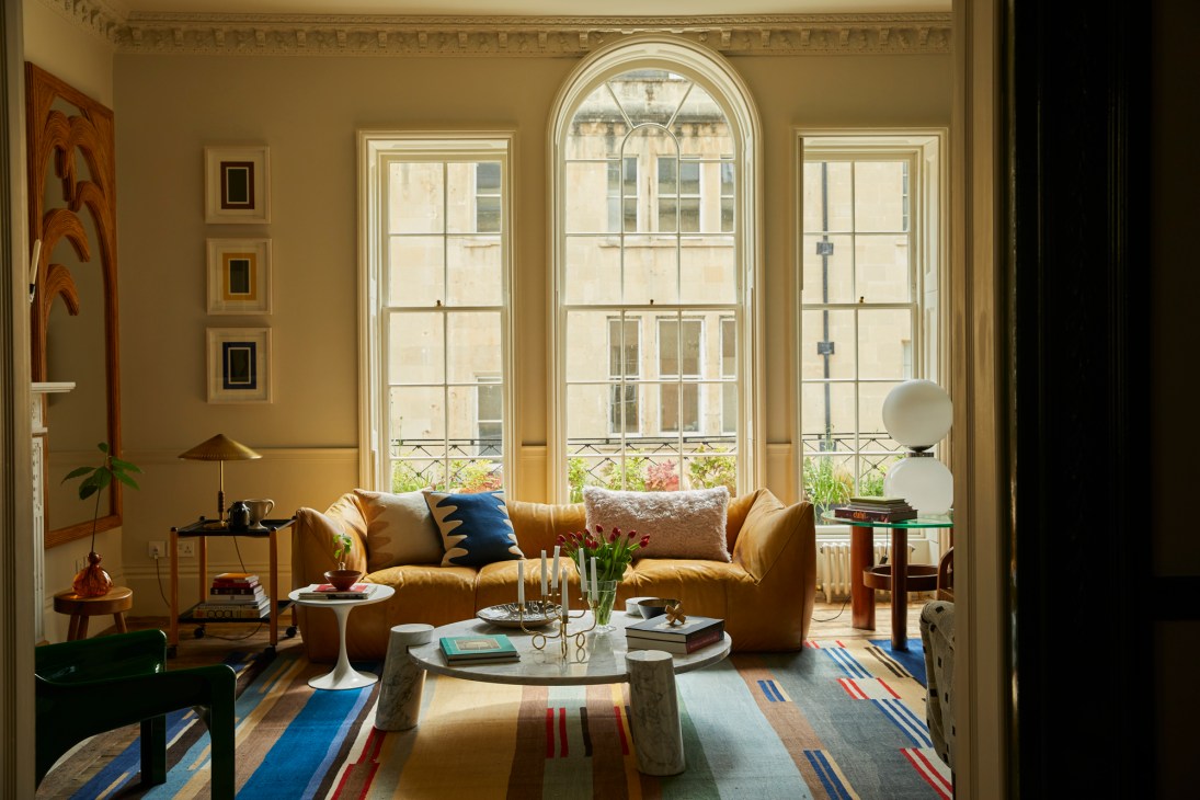 Living room with large mustard yellow sofa, colorful striped rug, and tall windows in Georgian townhouse
