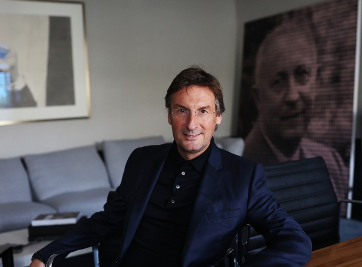 Pietro Beccari sitting at a wooden table in his office with contemporary artworks visible on the walls behind him