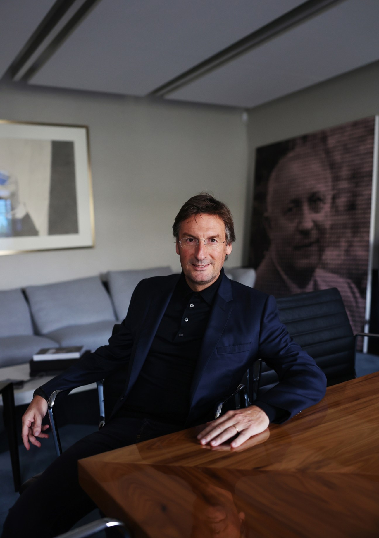 Pietro Beccari sitting at a wooden table in his office with contemporary artworks visible on the walls behind him