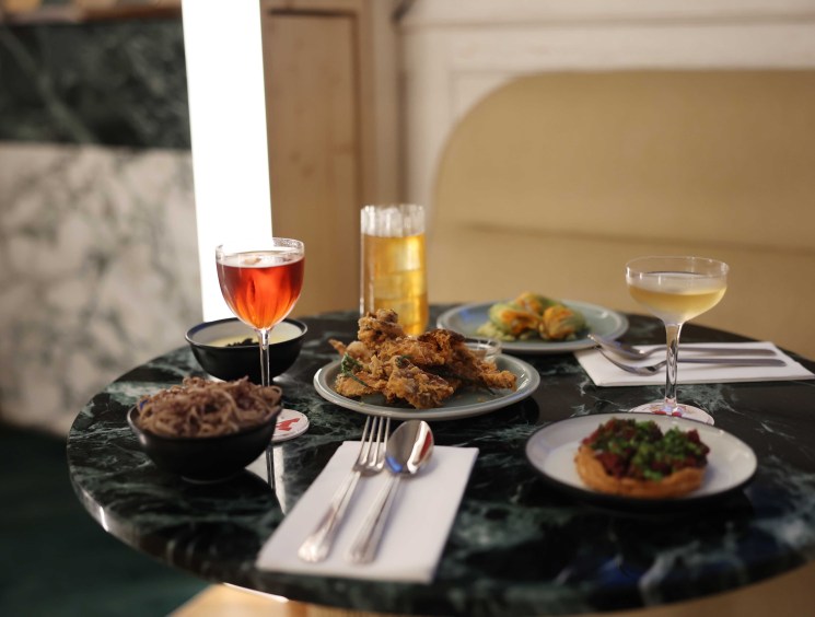 Elegant dining spread on marble table with cocktails, fried chicken, and small plates in upscale restaurant setting