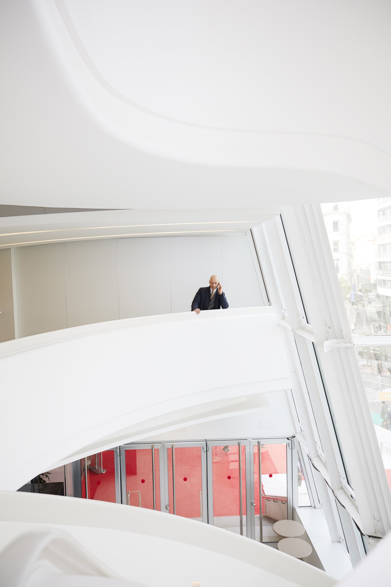Person in suit speaking on phone at modern white architectural interior with curved balconies and red accent wall