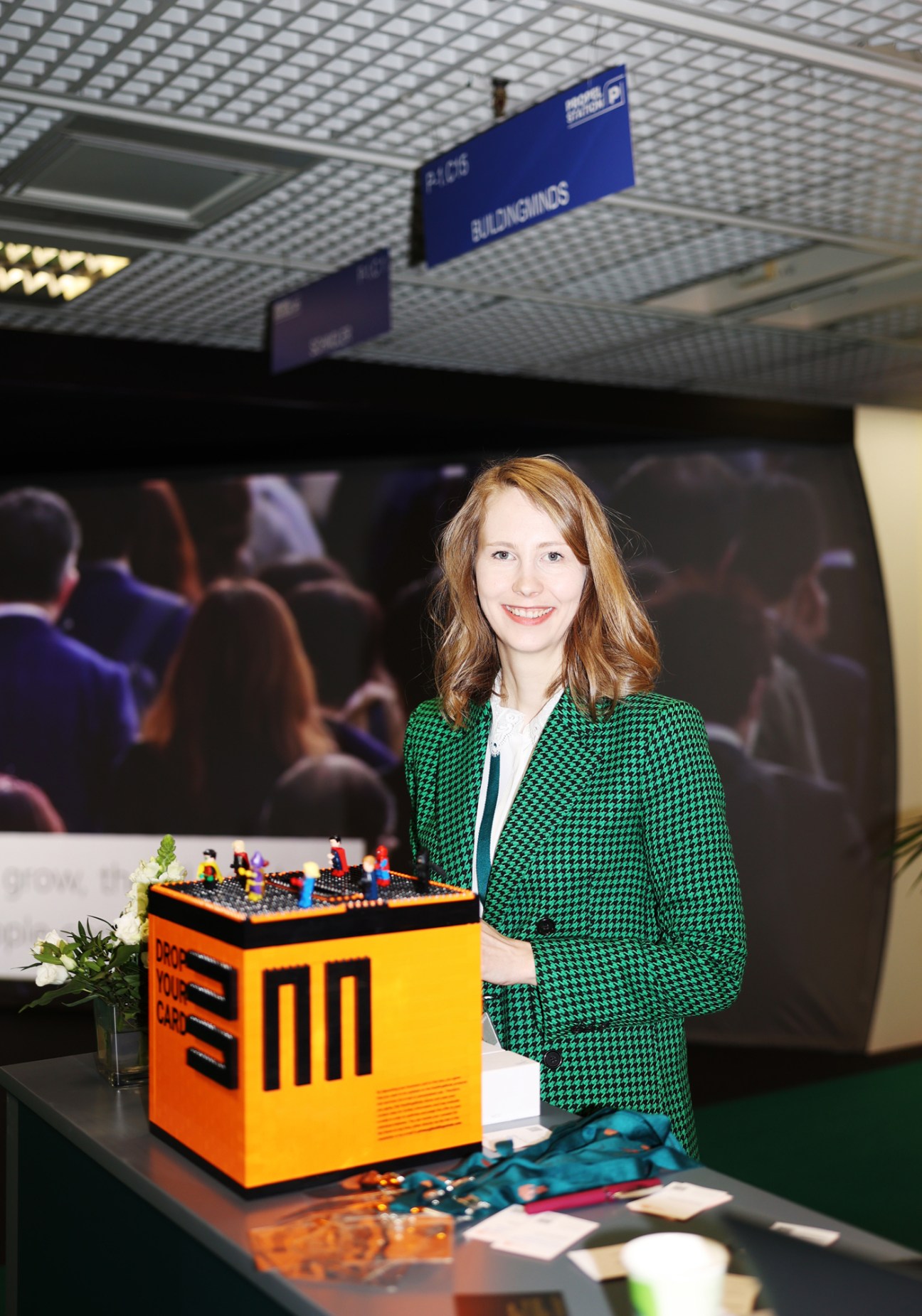 Woman in green houndstooth blazer standing beside orange electronic device at property conference
