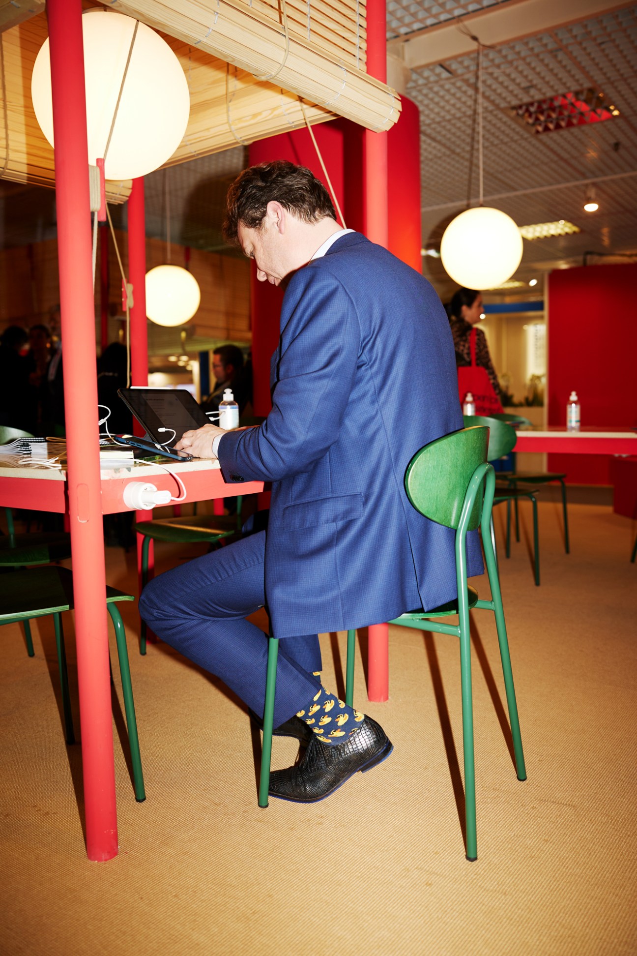 Man in blue suit working on laptop at modern office desk wearing colorful duck-patterned socks