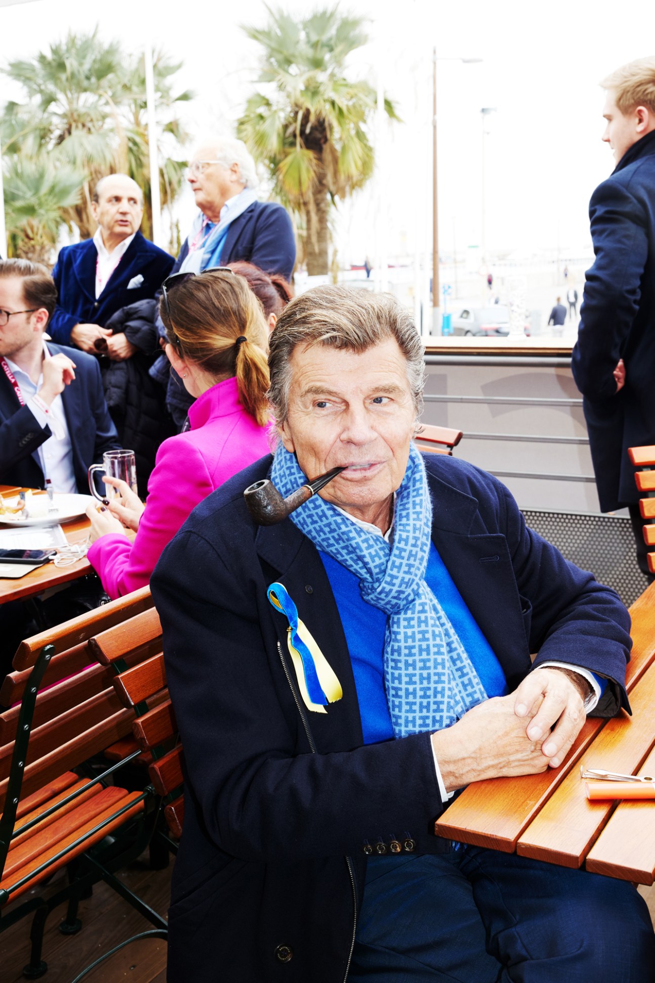 Stylishly dressed man with pipe and blue patterned scarf at outdoor cafe table during Mipim property conference