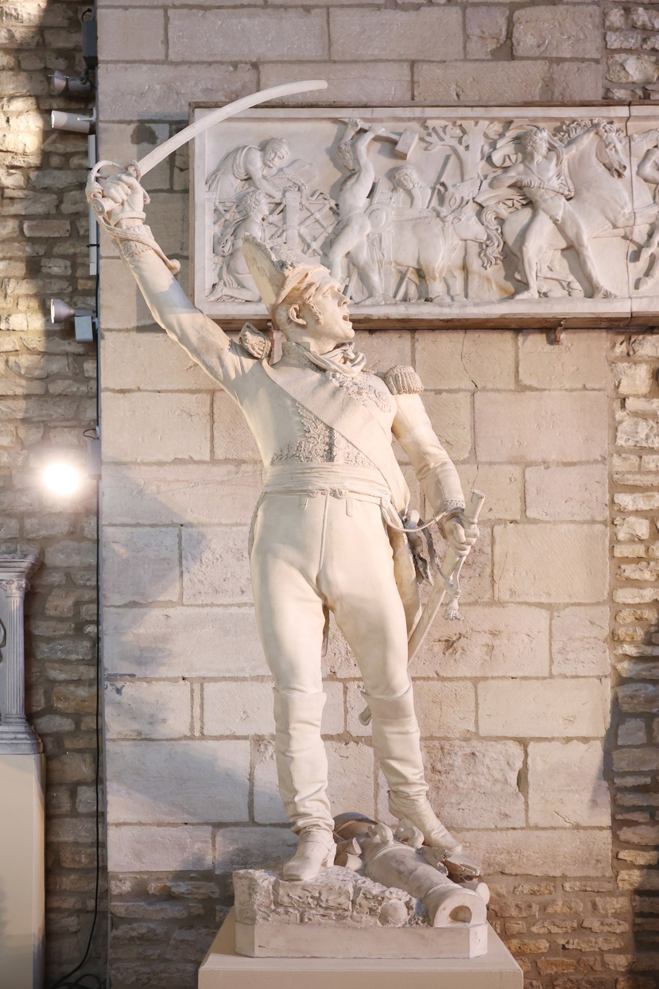 Stone statue of a historical figure with bow and arrow against a relief carving on a building facade in Dijon