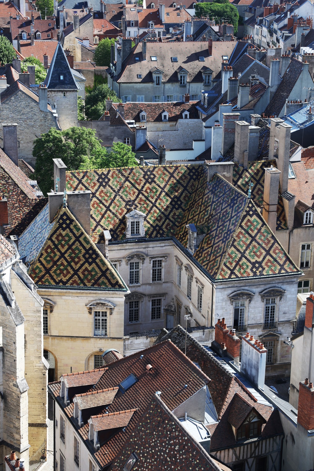 Aerial view of colorful geometric patterned tile rooftops on historic buildings in Burgundy, France