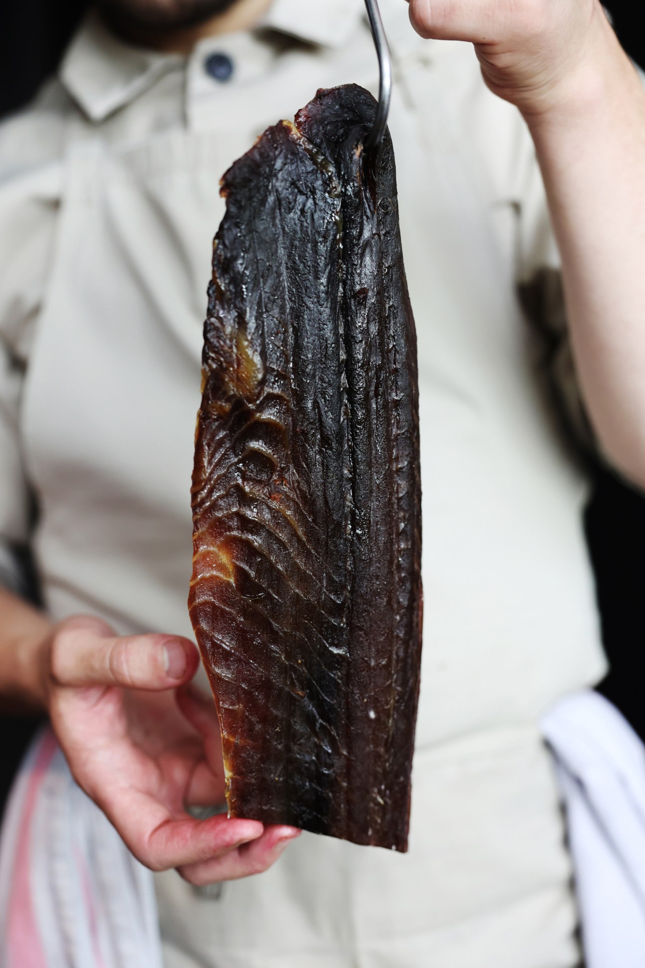 Chef in white uniform holds a large piece of dark, glossy smoked fish with distinctive scale patterns
