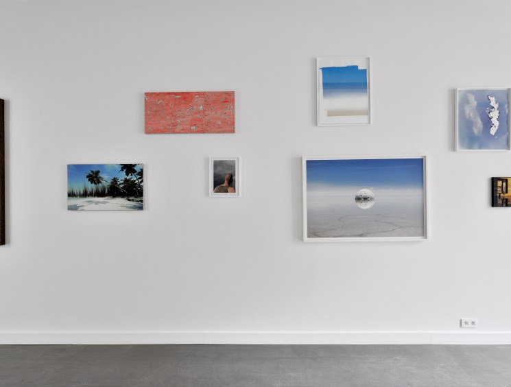 Gallery wall displaying various framed artworks including landscapes, abstract pieces and photographs in white frames