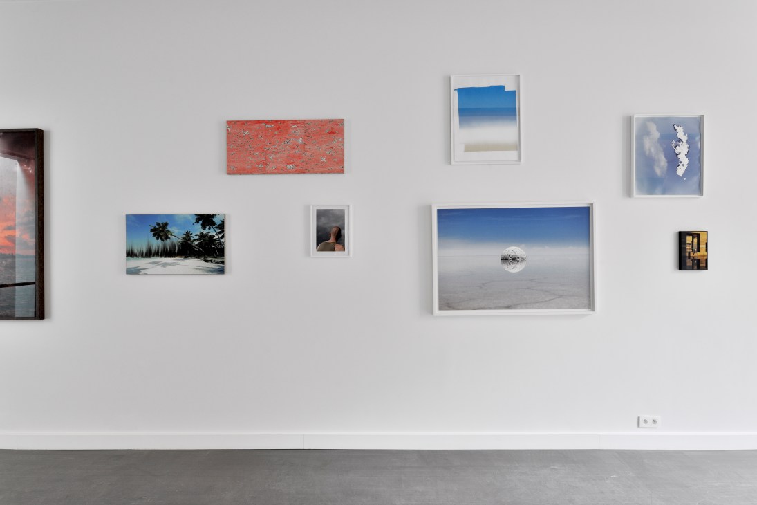 Gallery wall displaying various framed artworks including landscapes, abstract pieces and photographs in white frames