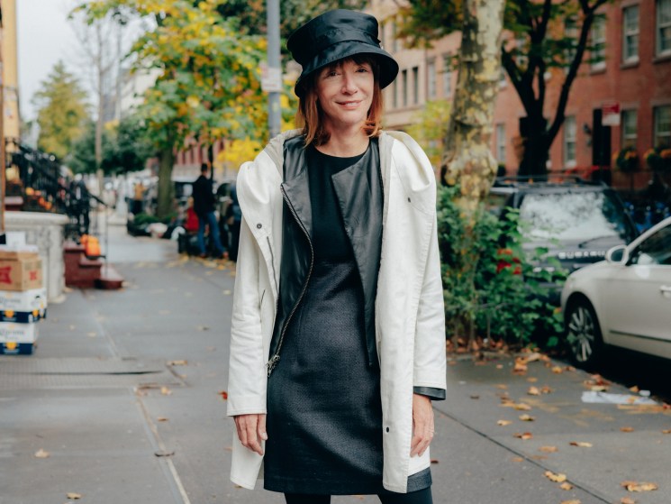 Woman in black bucket hat and white coat standing on autumn street with fallen leaves