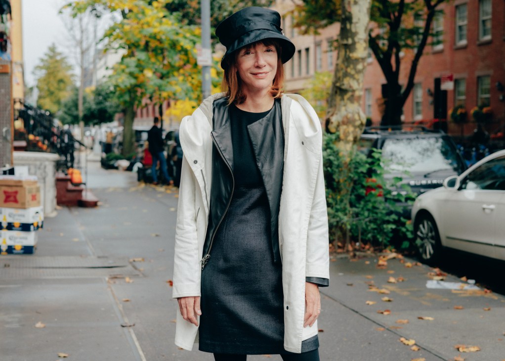 Woman in black bucket hat and white coat standing on autumn street with fallen leaves