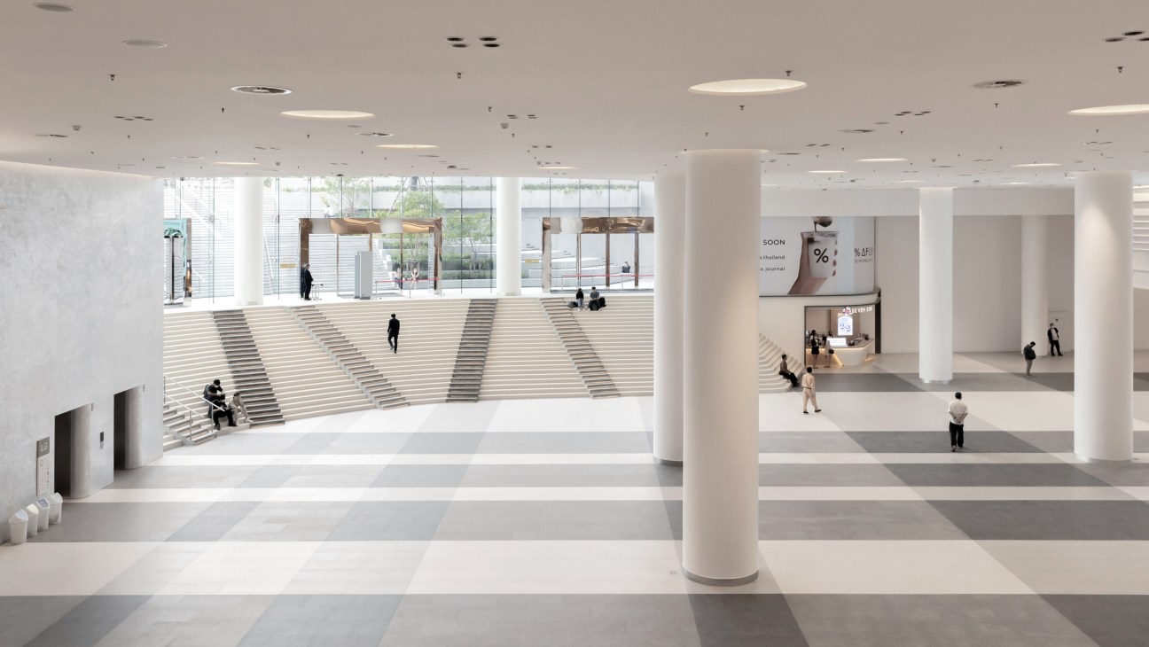 Modern interior space with white columns, multiple levels, and people walking through a bright atrium-like area