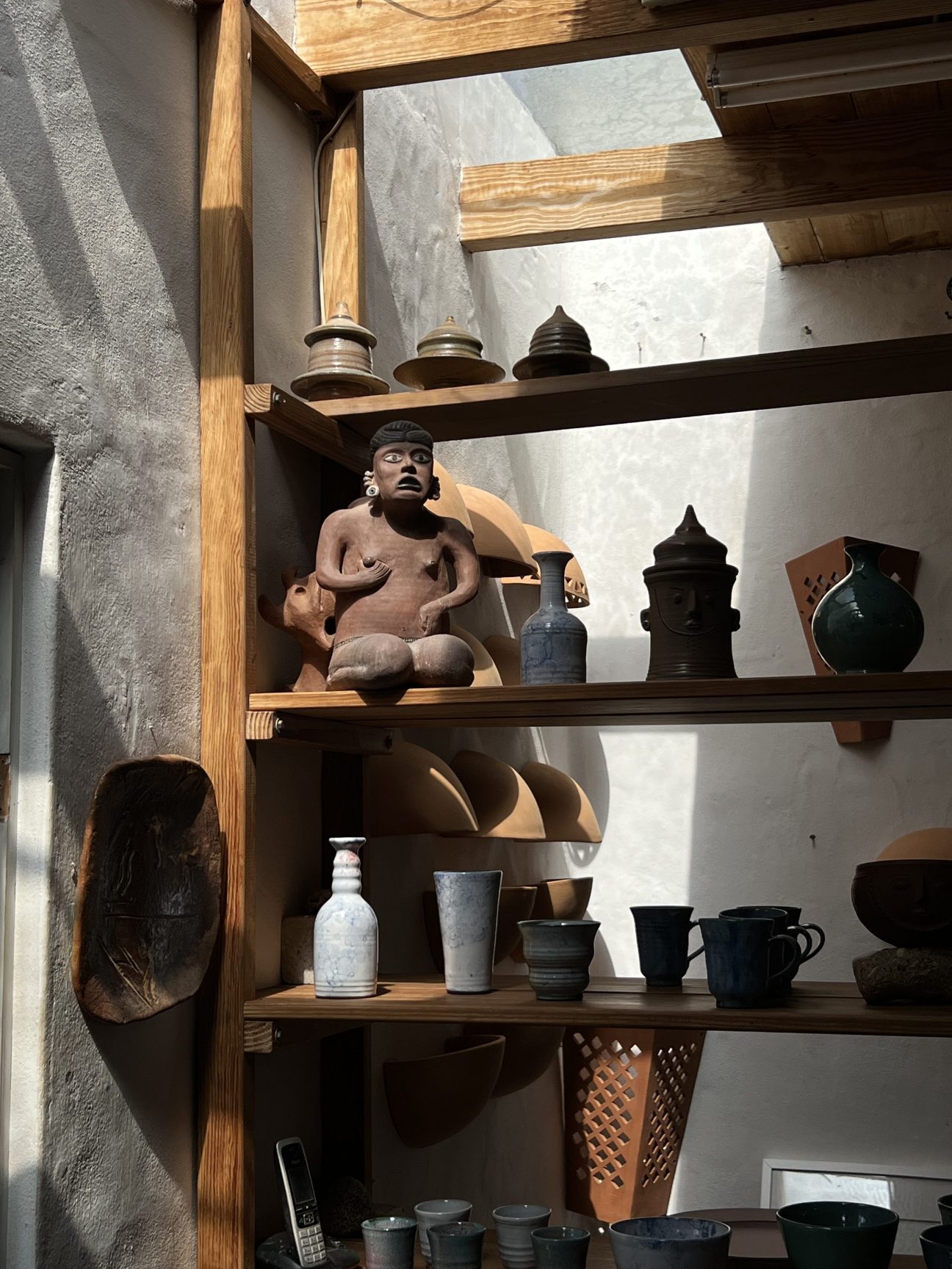 Wooden shelves displaying ceramic pottery, sculptures and vessels in a pottery studio workspace