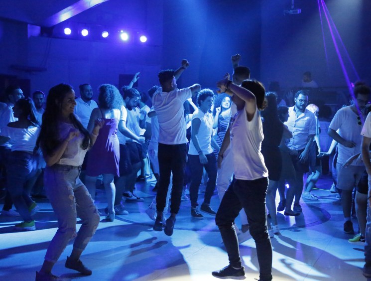 A crowd of people dancing under blue stage lights at an indoor party or event.