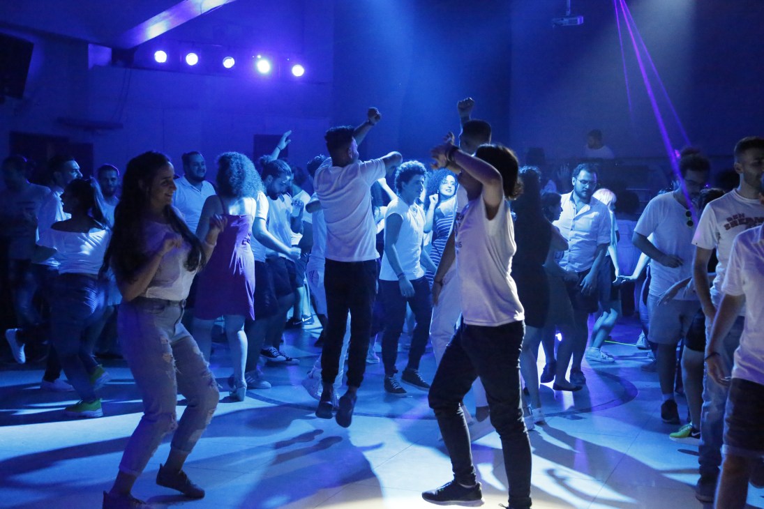 A lively crowd dancing energetically on a dance floor under blue and purple party lights.