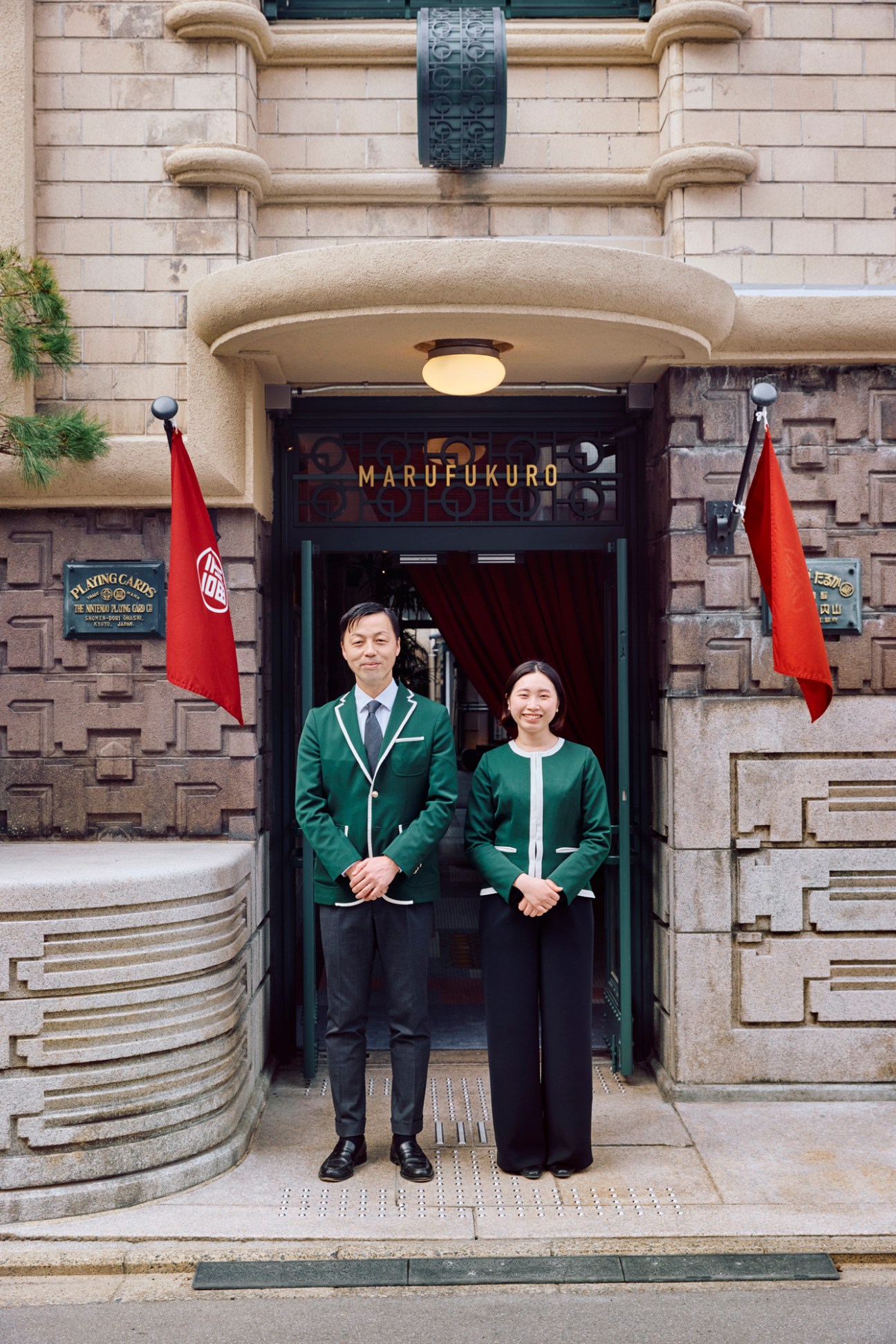 Two hotel staff members in matching green uniforms standing at the entrance of Marufukuro hotel