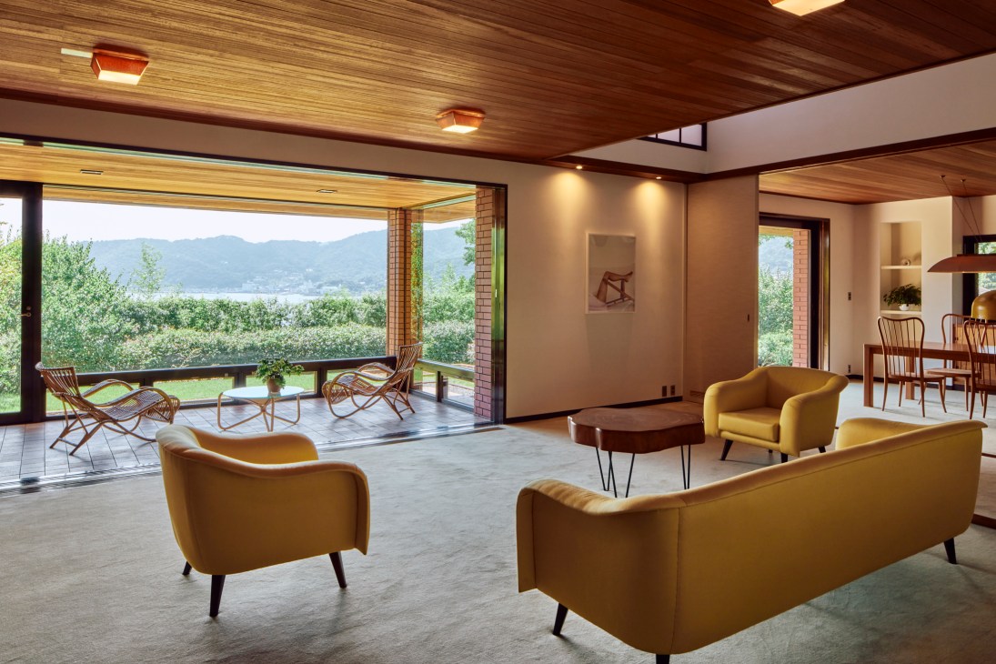 Modern living room with yellow Joaquim Tenreiro sofa and armchairs, wood ceiling, and mountain views through large windows