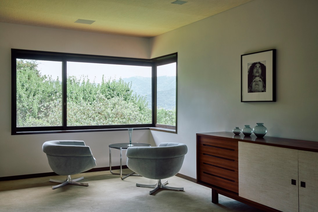 Modern interior corner with gray swivel chairs, glass side table and wooden credenza near large windows