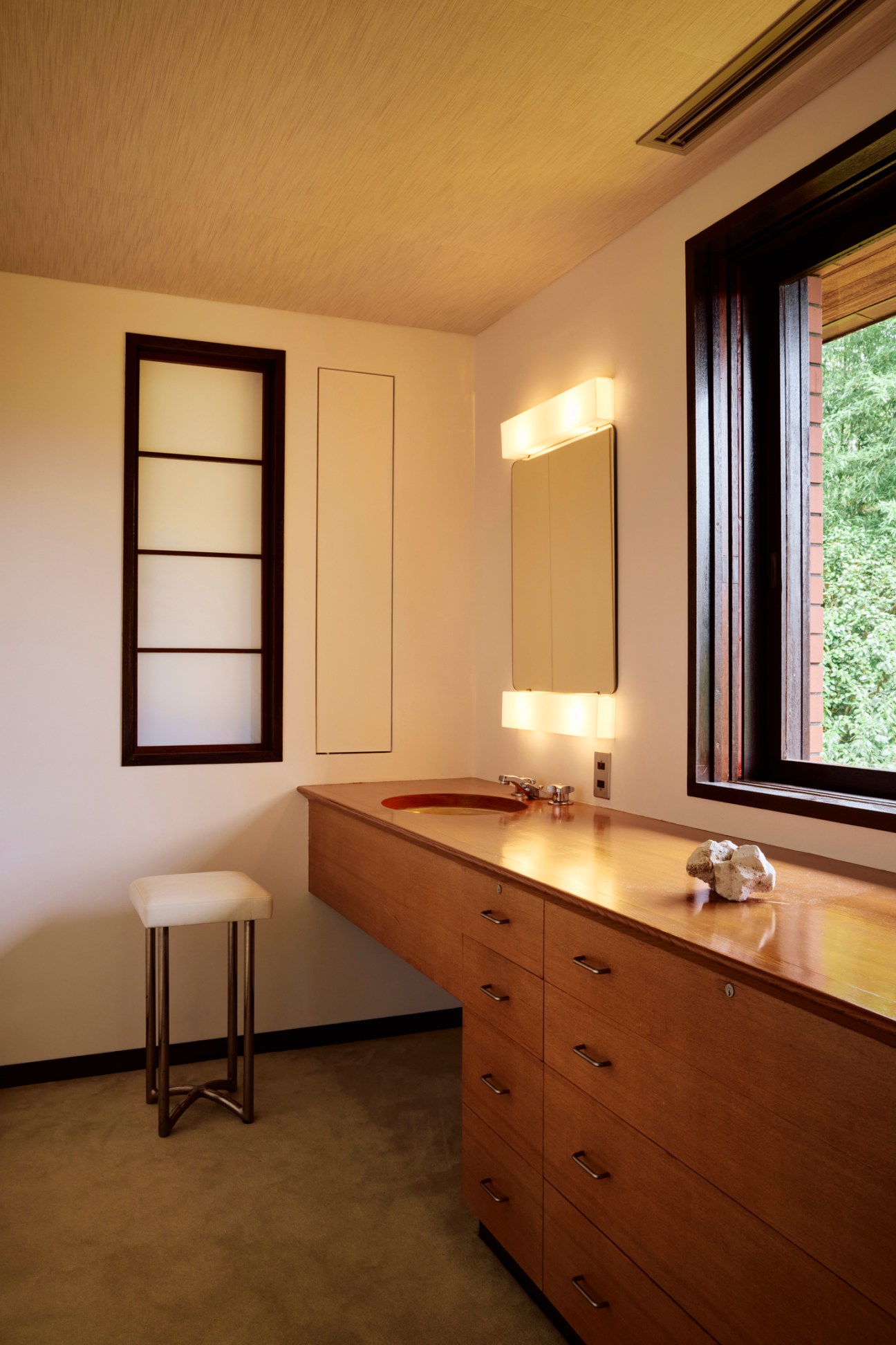 Modern bathroom vanity with wood cabinetry, integrated sink, illuminated mirror and white stool