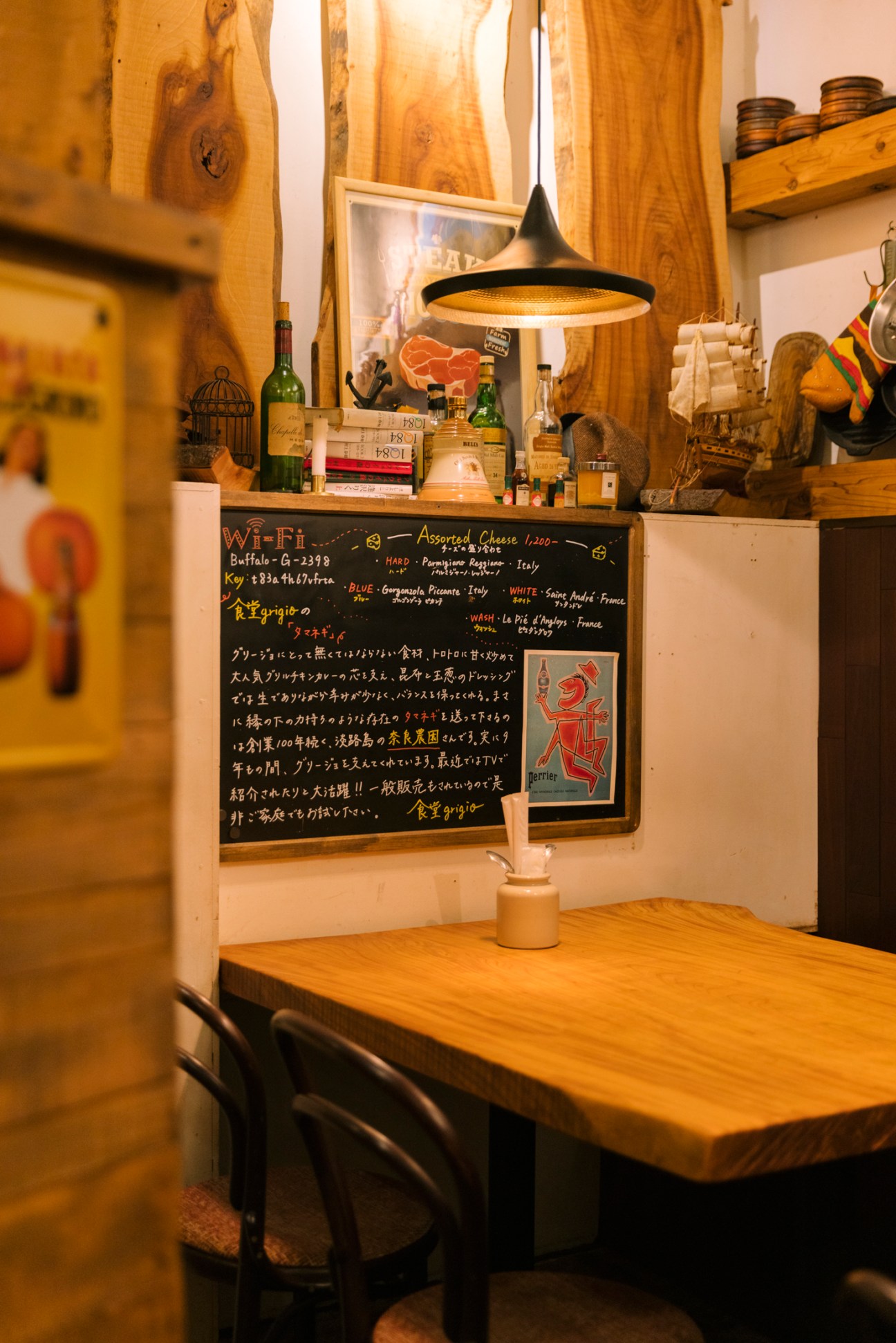 Interior of Grigio restaurant showing wooden table, blackboard menu with Japanese text, wine bottles and pendant lighting