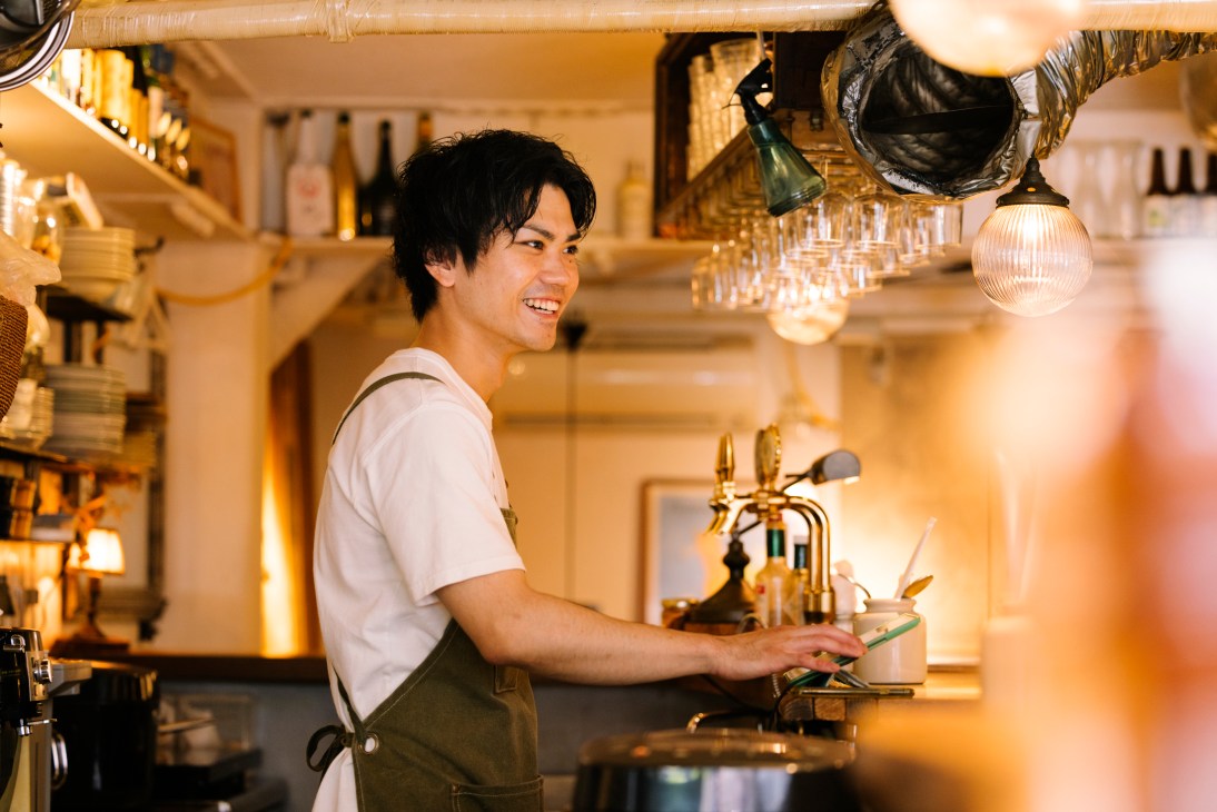 Smiling man in apron working behind bar counter at Grigio restaurant in Tokyo