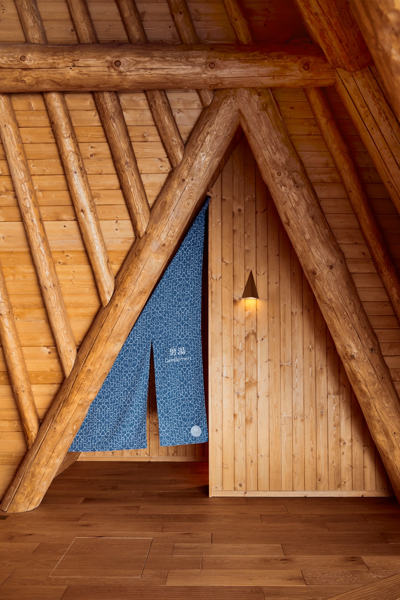 Distinctive cone-shaped wooden bathhouse structure with copper detailing set against winter landscape