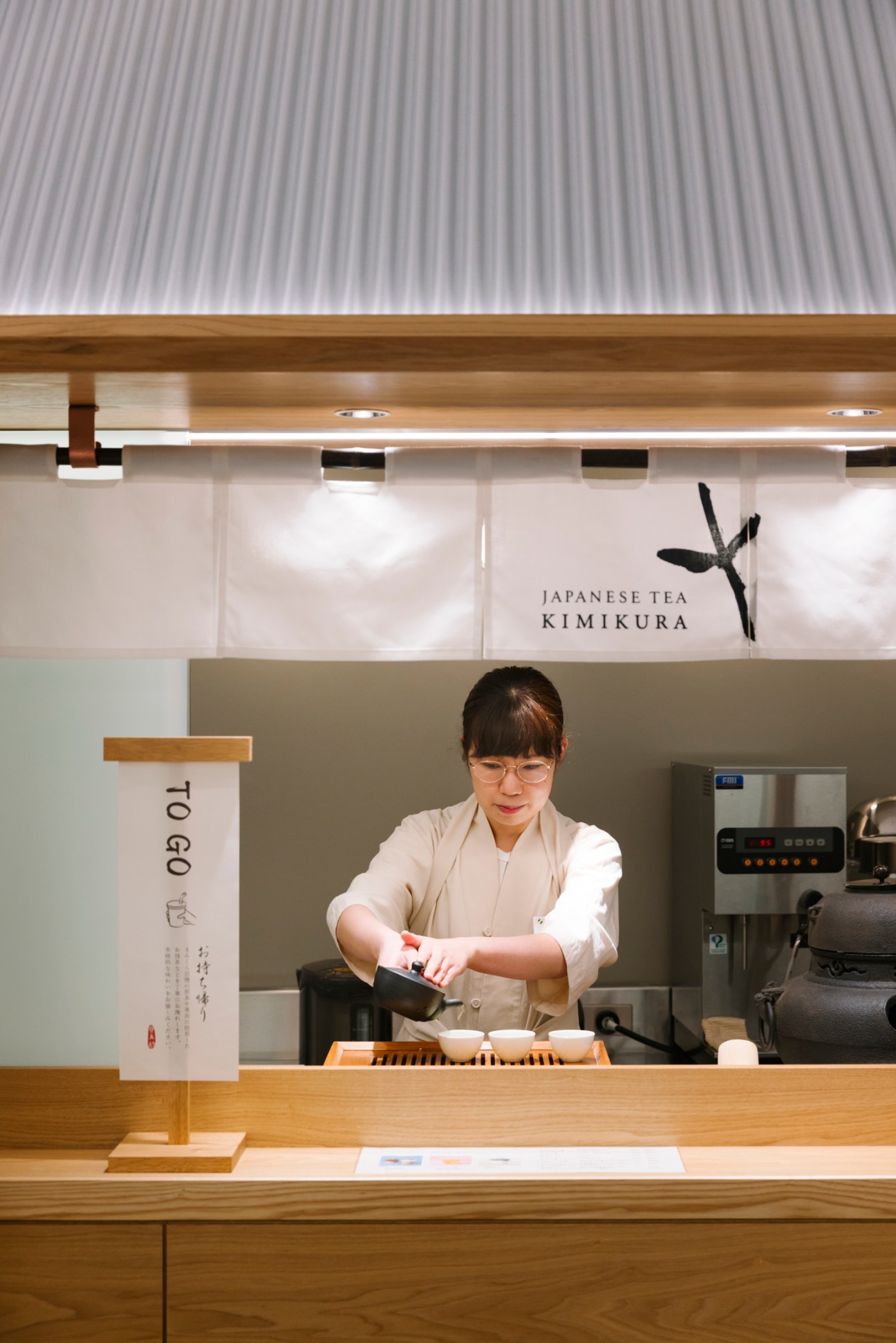 A woman in traditional white clothing prepares tea at a modern Japanese tea counter at Kimikura shop