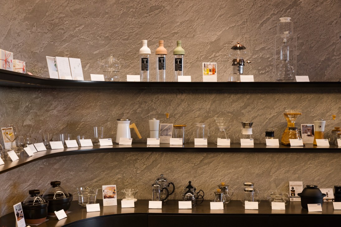 Three shelves display various coffee brewing equipment including glass carafes, pour-over devices, and teapots with price tags