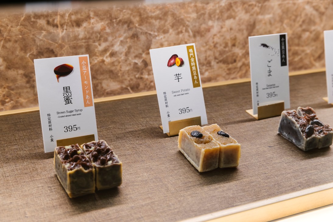 Three Japanese confections displayed on wooden tray with white price cards showing flavors and 395 yen prices