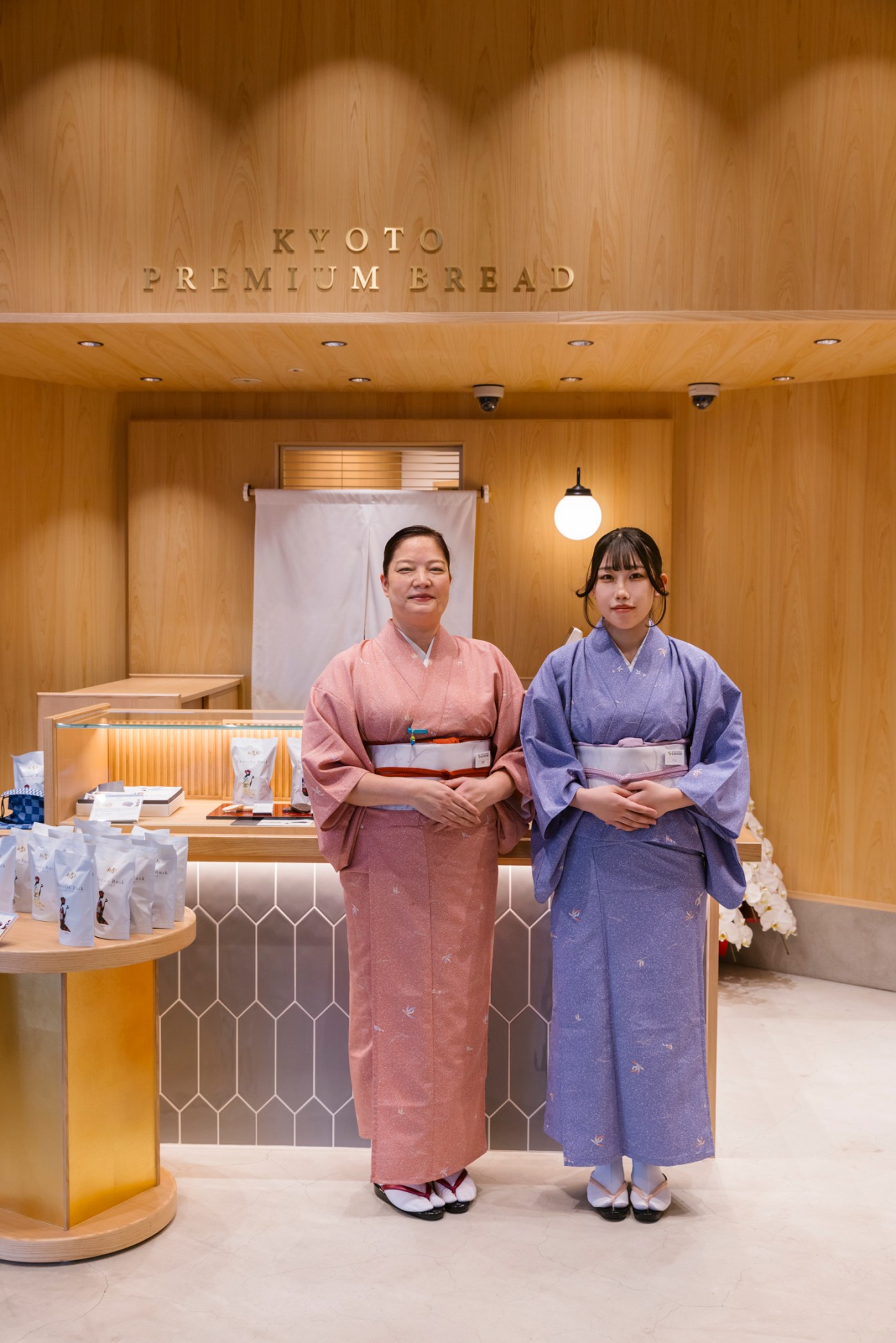 Two women in traditional Japanese kimono standing in front of Kyoto Premium Bread bakery storefront
