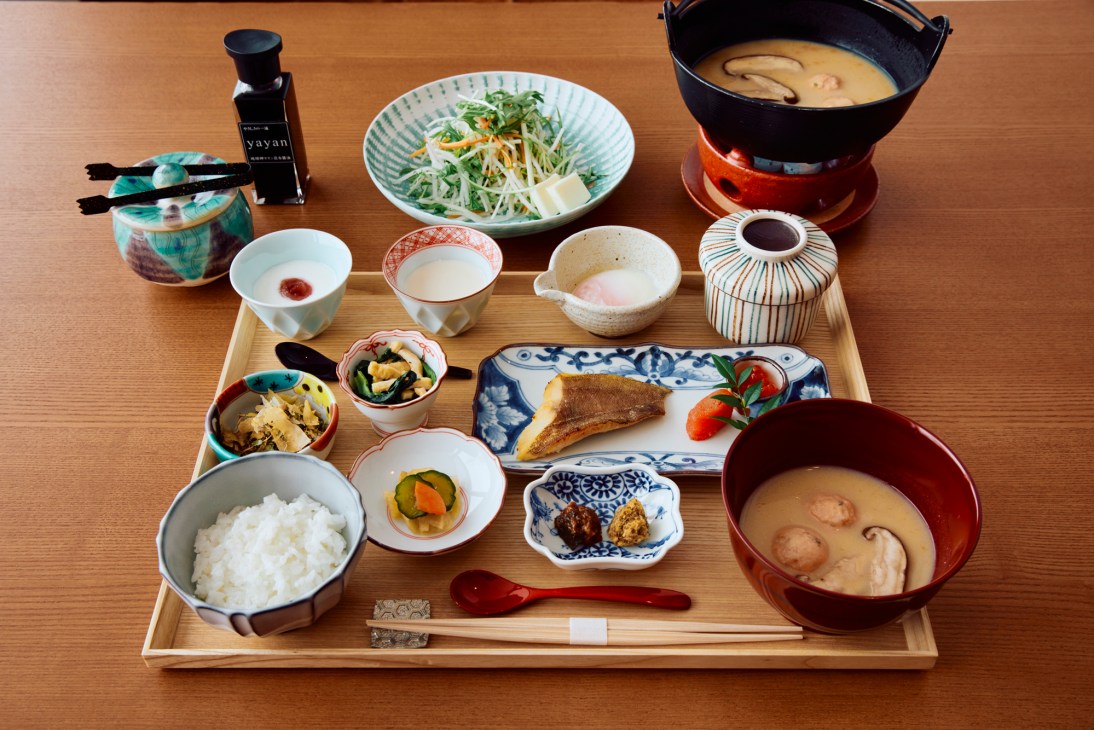 Traditional Japanese breakfast spread with multiple small dishes, rice, and soup arranged on wooden table