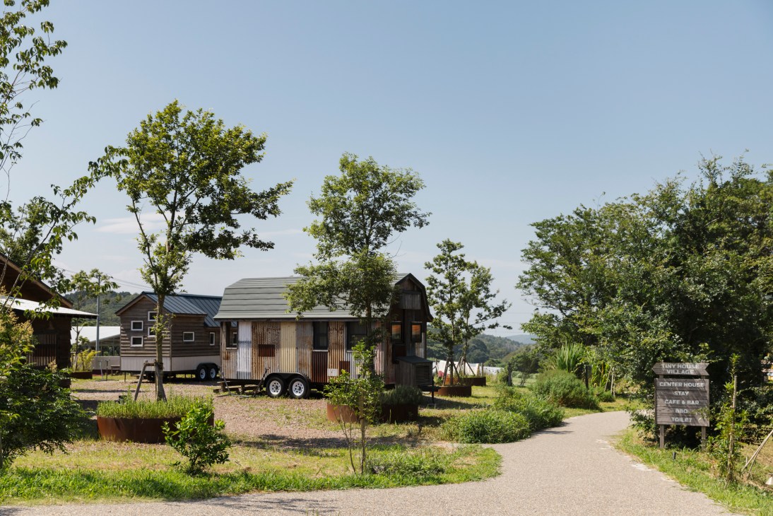 Small wooden tiny houses on wheels parked in a rural campground setting surrounded by mature trees