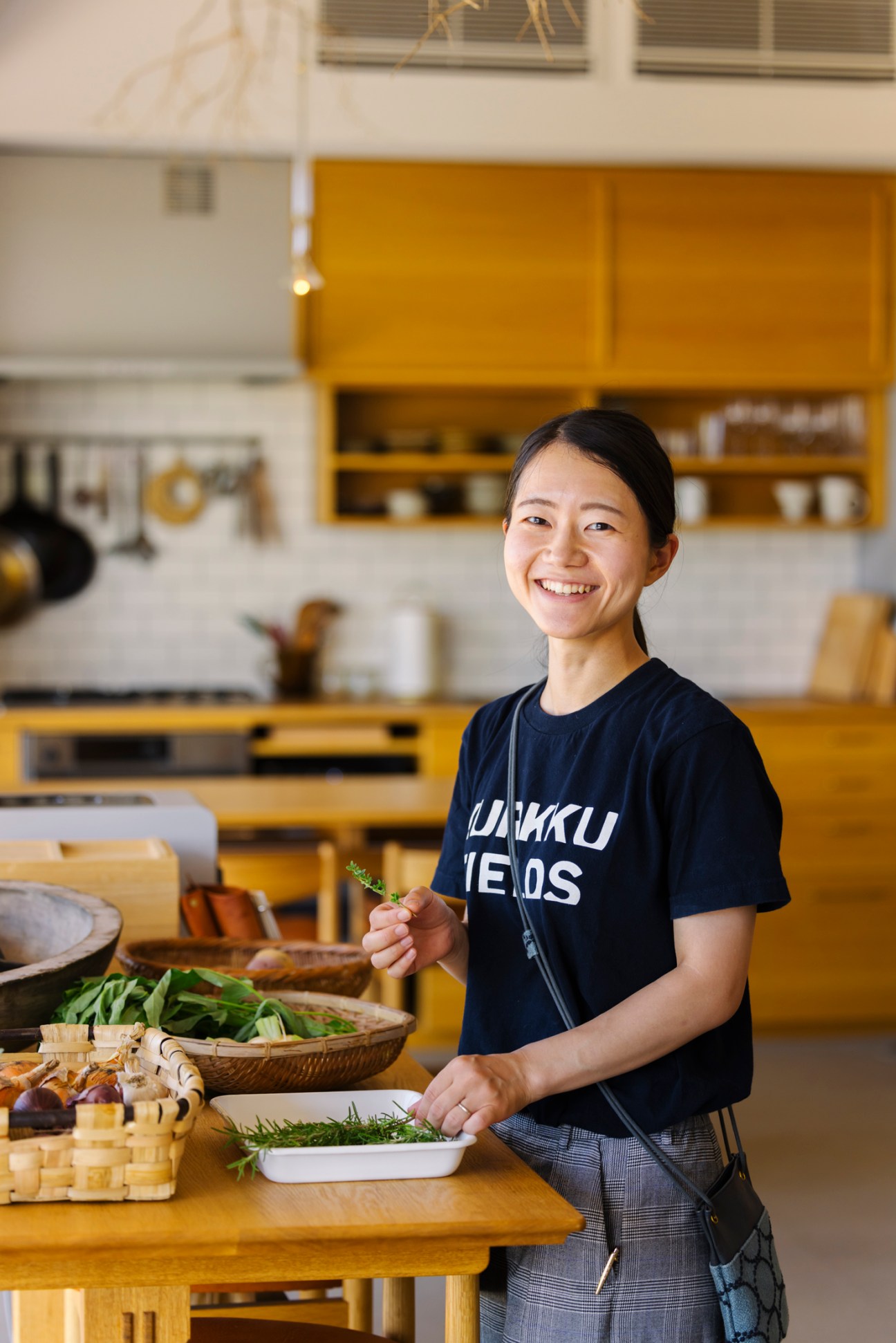 Smiling woman in kitchen preparing fresh vegetables and herbs on wooden counter at Japanese retreat