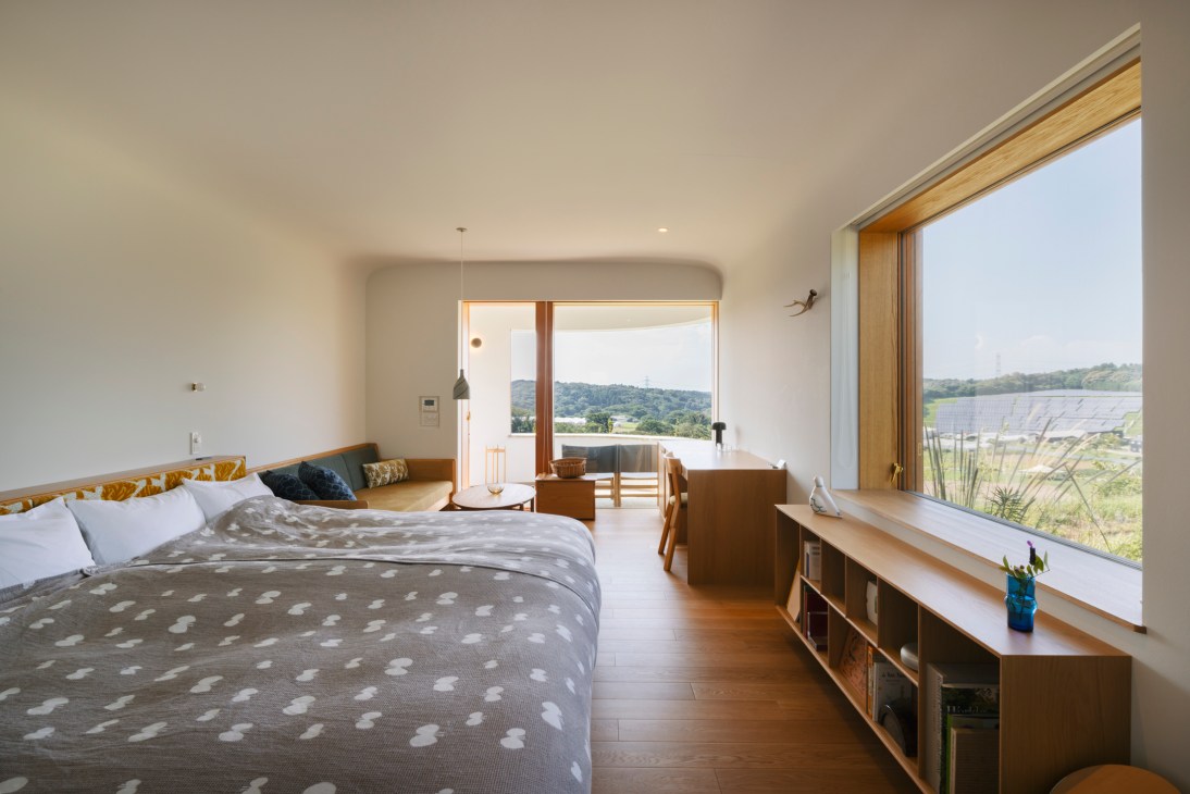 Modern bedroom with wooden furniture, large windows overlooking countryside, and polka dot bedding
