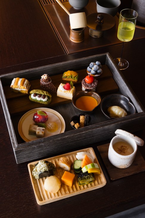 Elegant Japanese kaiseki meal presentation with colorful petit fours, sushi, and traditional sweets in wooden boxes