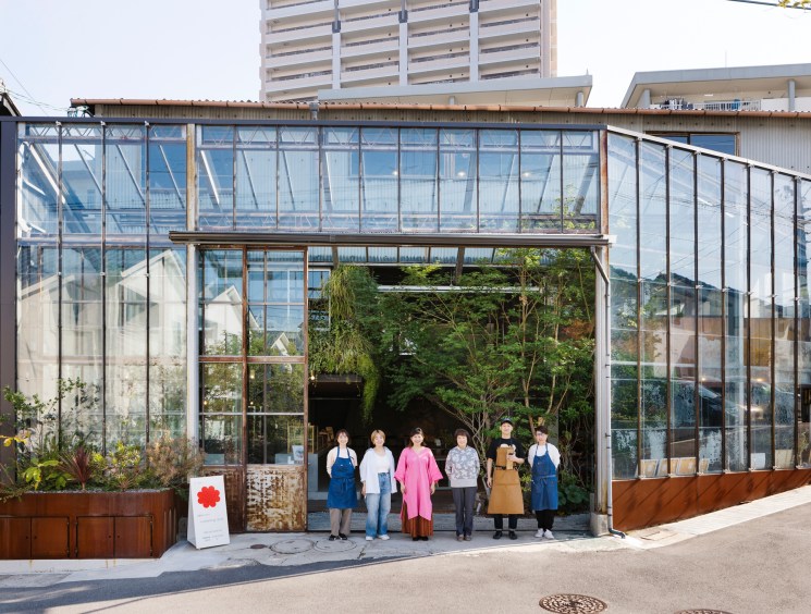 Six people in aprons standing together outside glass greenhouse-style building at Minagarten development