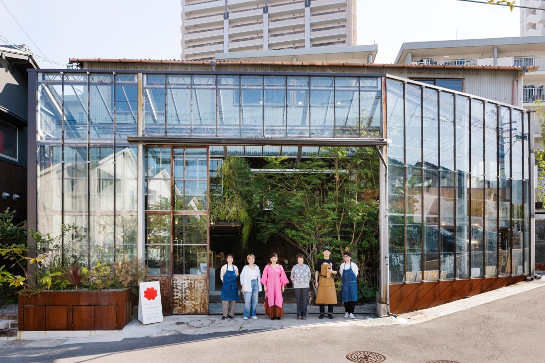 Six people in aprons standing together outside glass greenhouse-style building at Minagarten development