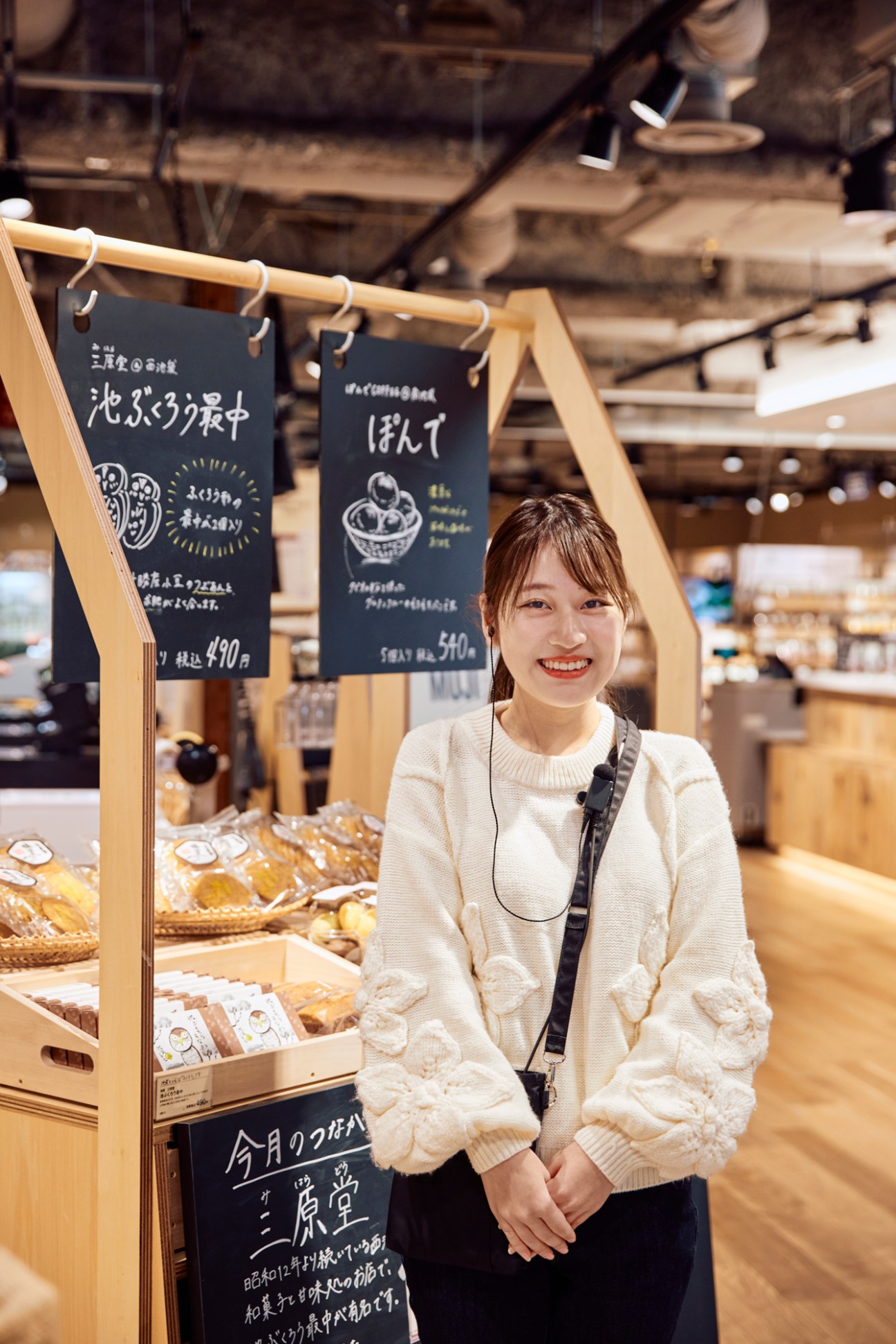 Smiling woman in white sweater stands next to food display with Japanese signage in retail setting