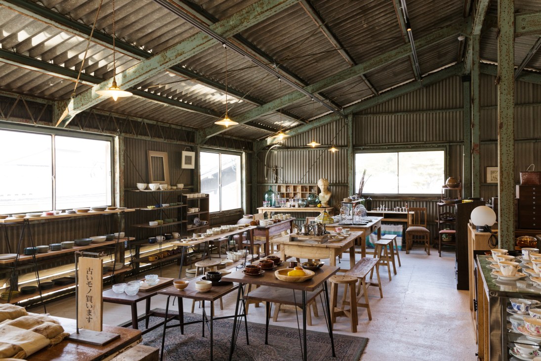 Interior of renovated warehouse showing corrugated metal ceiling, pendant lights, and pottery workshop with tables and ceramics
