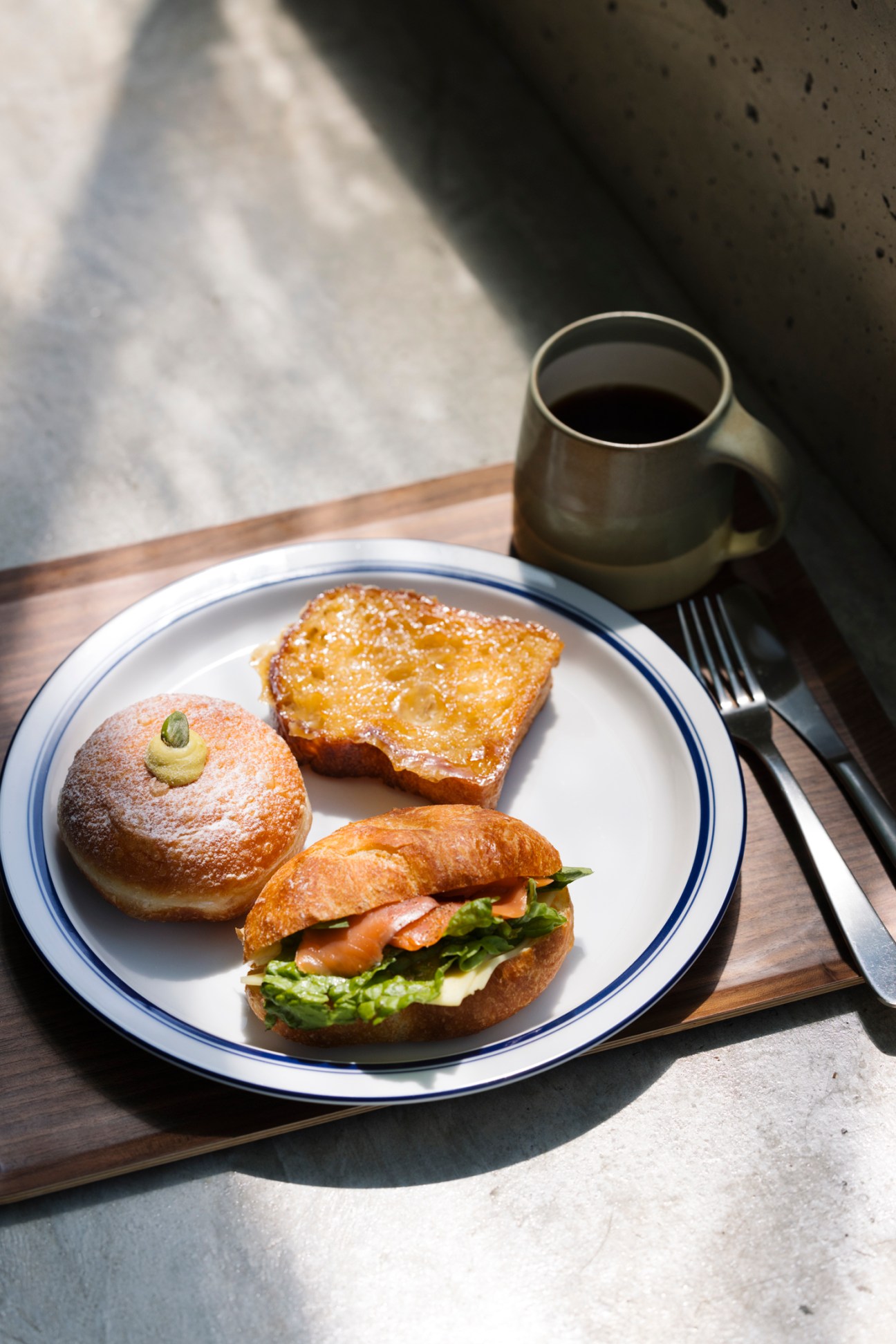 Plate with pastries and sandwich alongside coffee cup on wooden tray