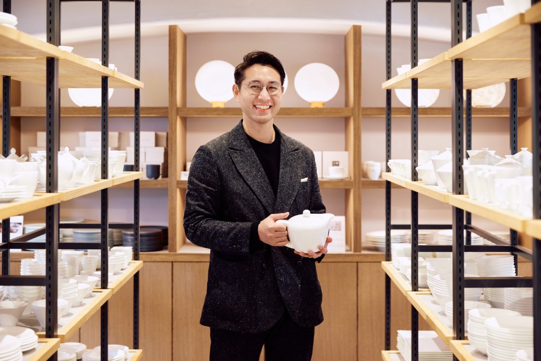 Naoki Mitani standing in porcelain showroom holding white bone china teapot surrounded by shelves of white tableware
