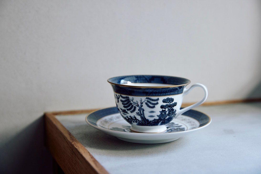 Traditional blue and white willow pattern china teacup and saucer on wooden tray