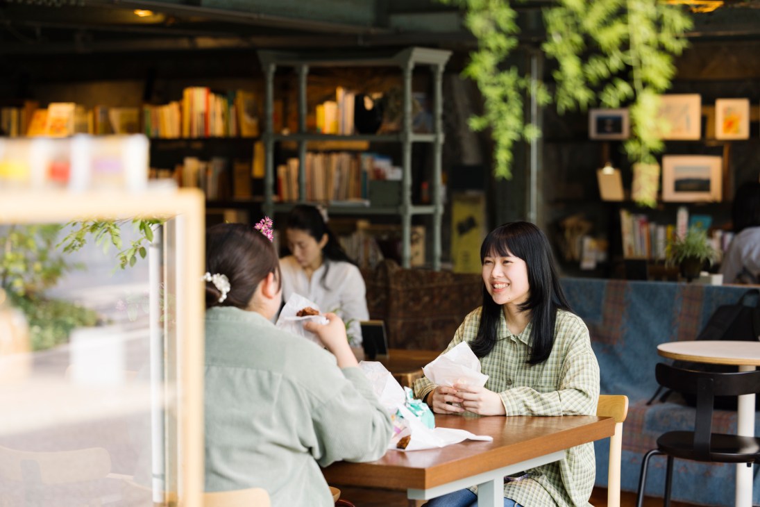 Two people sitting at a table having a conversation in a bookstore cafe with bookshelves in the background