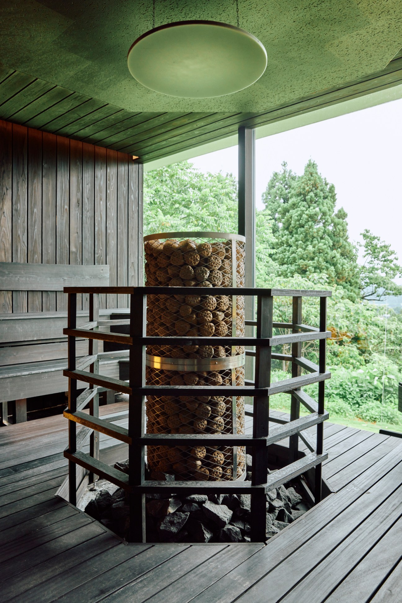 Traditional Finnish-style sauna interior with wooden benches, protective metal screen around heater, and forest views through large windows