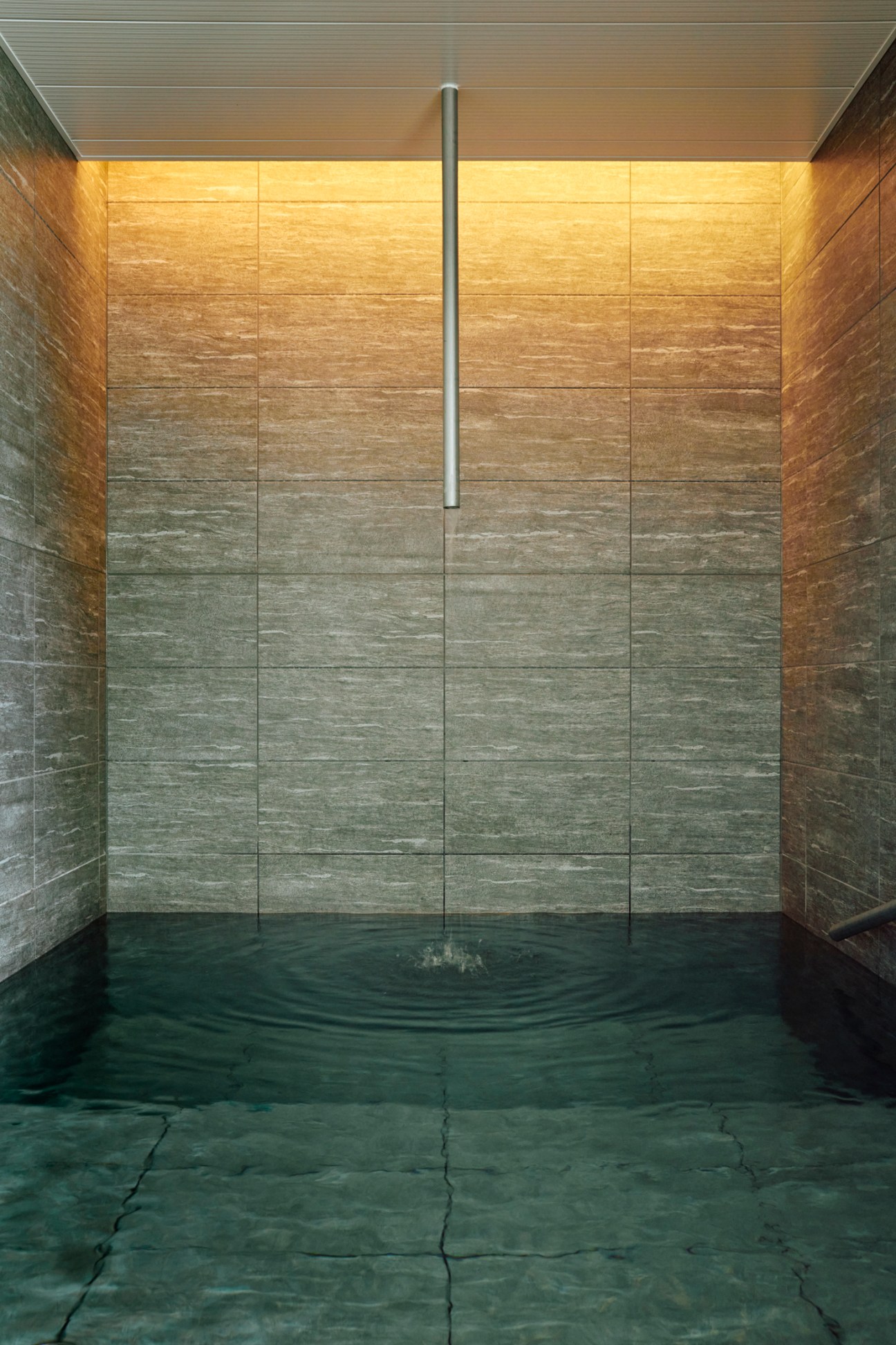 Circular plunge pool with rippling water surrounded by stone tiles and wooden paneled walls in spa interior