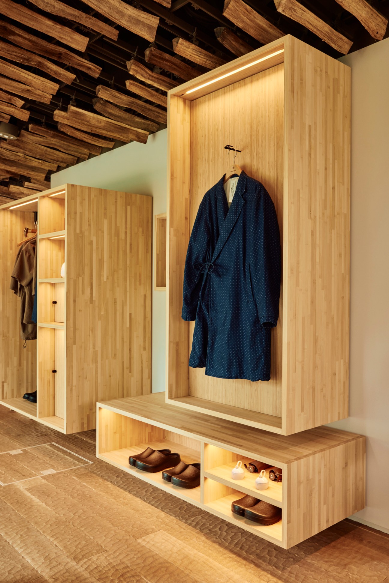 Traditional Japanese-style dark blue spa gown hanging on wooden rail with built-in lighting displaying and organized shoe storage below