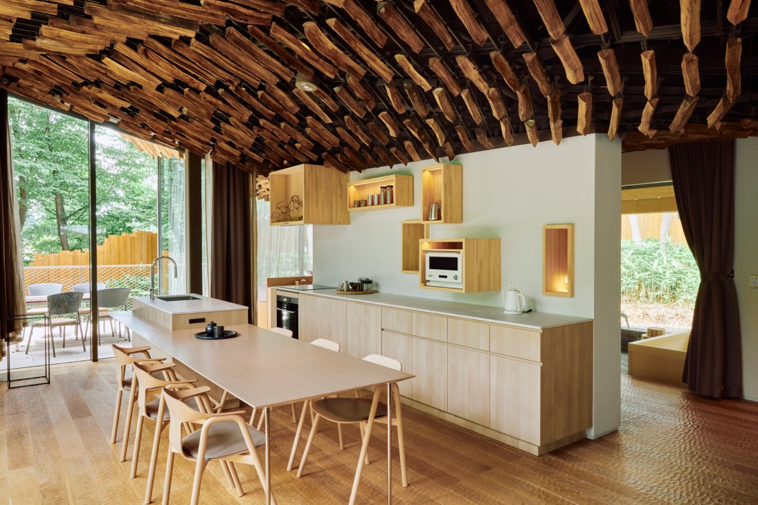 Modern kitchen with light wood cabinets, dining table, and distinctive wooden beam ceiling in contemporary interior